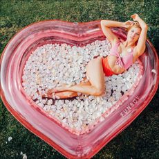 Woman posing in pink heart-shaped inflatable pool with flower petals